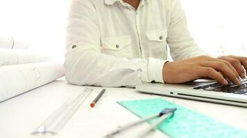 Architect sitting at desk research on laptop and developing project, man drawings on large format paper from internet, selective focus video