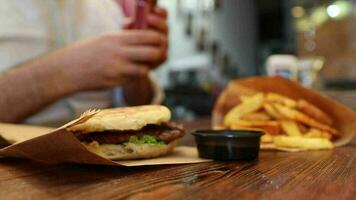 Sauce being poured on a green lettuce leaf resting on a burger, an image of man-eating fast food in restaurant video