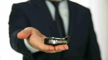 Businessman in a suit standing in front of the white background showing the ignition in his palm and the way he turned it on to the camera video