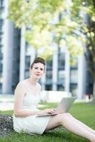 Young woman using tablet outdoor sitting on grass, smiling. photo