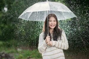 contento asiático niña con transparente paraguas entre el lluvia foto