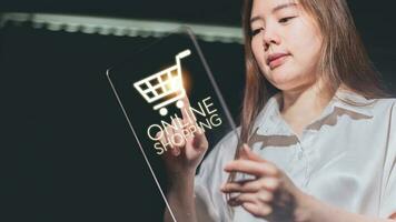 joven asiático mujer utilizando tableta con compras carro icono. en línea compras concepto. foto