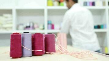 Colored rolls of thread used for sewing, tailor taking threads in sewing workshop and laying them on shelves, selective focus video