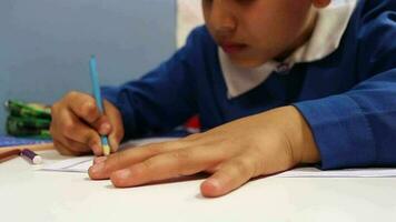 Garoto dentro escola uniforme pintura às mesa, pequeno Garoto desenha com coloração lápis, seletivo foco video