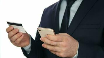 Man in a suit standing in front of white background uses online banking with the hairy phone, easy payment using a smartphone or digital device video