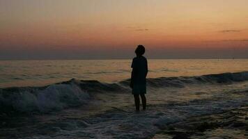 image de une déprimé et réfléchi homme par le mer à coloré coucher de soleil, le silhouette de une homme permanent dans rugueux mer video