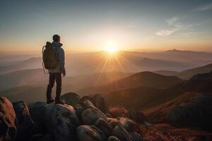 A male hiker stands on the peak of a cliff high in the mountains and looks out at the sunset. photo