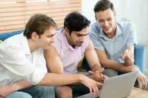 Triple young man sitting in the living room while using laptop to video call with rainbow flag on desk. LGBTQ people lifestyle and love emotion. LGBT social network. selective focus photo