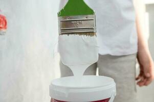 The child holds a paint brush with white paint. Lower the brush into the paint jar. photo