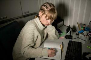 An overworked student sits at the computer at night. Make notes in a notebook in the dark. photo