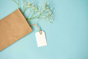 A mock-up of a white tag and a price tag near a craft package with flowers lie on a blue table photo