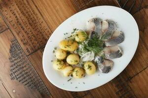 arenque pescado con joven patatas pelotas en un blanco plato foto