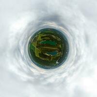 green tiny planet in blue overcast sky with beautiful clouds with transformation of spherical panorama 360 degrees. Spherical abstract aerial view. Curvature of space. photo