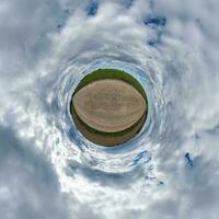 tiny planet in blue overcast evening sky with beautiful clouds with transformation of spherical panorama 360 degrees. Spherical abstract aerial view. Curvature of space. photo