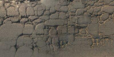 top view of surface of asphalt road made of small stones and sand with cracks photo