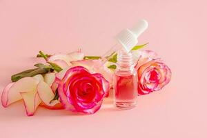 Bottles with rose essential oil and flowers on marble table photo