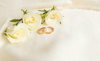 dos oro Boda anillos y Tres té rosas en un satín antecedentes con perla rosario. un Copiar de el espacio. Boda antecedentes. tarjeta postal. diseño disposición. foto