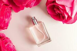 A transparent bottle of women's perfume or eau de toilette lies among the large buds of pink roses. Top view. Template for product presentation. photo