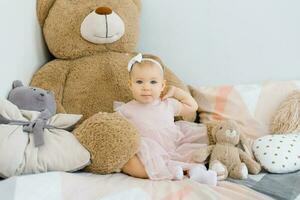 A cute one year old baby sits surrounded by soft animals toys and pillows photo