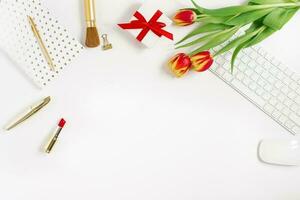 Postcard for Valentine's Day, Mother's Day or March 8. A bouquet of tulips, a gift with a red bow, a keyboard and mouse, cosmetics and a notebook with a pen. Falt lay blogger with copy space photo