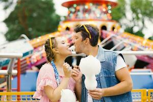 contento Pareja en amor disfrutando cada otro en un diversión parque. un chico y un niña comiendo algodón caramelo y riendo foto
