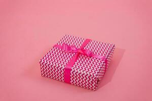 Gift box on pink background. A gift in bright paper, decorated with a stylish elegant fuchsia satin ribbon bow. The concept of Christmas and any other holidays photo
