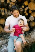 Portrait of a young dad and her child, whom she holds in her arms, sitting on logs in the forest in summer photo