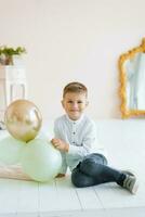 A child boy is sitting on the floor and holding balloons in his hand at home and smiling photo