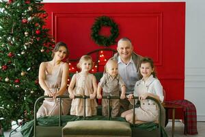 A stylish family with three children is sitting on a bed near a Christmas tree. A cozy Christmas holiday photo