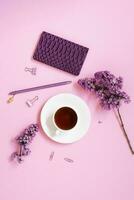 un taza de té, cuadernos, un bolígrafo, un ramo de flores de lilas en un púrpura antecedentes. púrpura primavera flores composición para un blogger o negocio foto