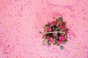 Beautiful bouquet of pink roses and eucalyptus branches in a gift basket on a pink background with confetti for a birthday, Valentine's day or mom's day. Top view from copy space photo