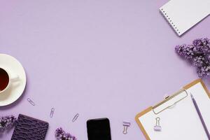 The workspace of a blogger or freelancer Flat lay with a cup of coffee, notebooks and lilac branches, stationery on a lilac background with a copy space photo