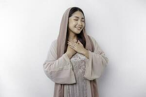 Happy mindful thankful young Asian Muslim woman with her hand on her chest smiling isolated on white background photo