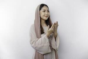 Religious beautiful Asian Muslim girl wearing a headscarf praying to God, isolated by white background photo