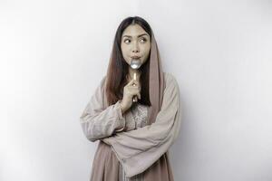 An Asian Muslim woman is fasting and hungry and holding cutlery while looking aside thinking about what to eat photo