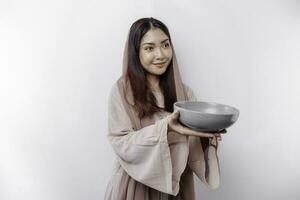 A smiling Asian Muslim woman is fasting and hungry and holding and pointing to a bowl photo