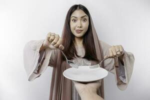 A smiling Asian Muslim woman is fasting and hungry and holding and pointing to a plate photo