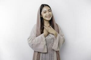 Happy mindful thankful young Asian Muslim woman with her hand on her chest smiling isolated on white background photo