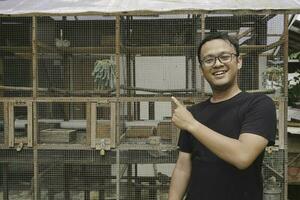 hermoso asiático hombre es sonriente y en pie en frente de pájaro jaula foto