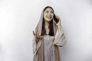 A happy Asian Muslim woman wearing a headscarf, happily talking on the phone, isolated by white background photo