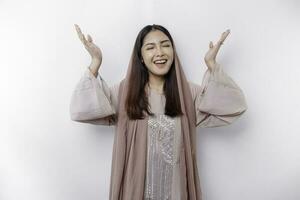 Excited Asian Muslim woman wearing headscarf pointing at the copy space above her, isolated by white background photo