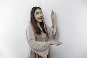 Shocked Asian Muslim woman pointing at the copy space on beside her, isolated by white background photo