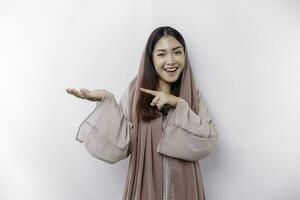 Young Asian Muslim woman smiling while pointing to copy space beside her photo