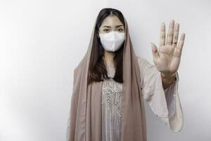 Young Asian Muslim woman wearing a mask and hijab shows her palm or stop gesture, covid prevention concept photo