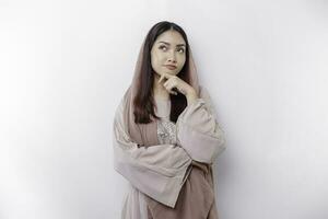 A thoughtful young Asian Muslim woman wearing headscarf while looking aside, isolated by a white background photo