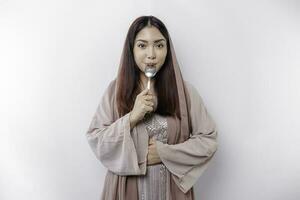 An Asian Muslim woman is fasting and hungry and holding cutlery while looking aside thinking about what to eat photo