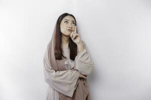 A thoughtful young Asian Muslim woman wearing headscarf while looking aside, isolated by a white background photo