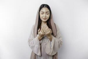 Religious beautiful Asian Muslim girl wearing a headscarf praying to God, isolated by white background photo