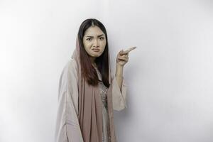 A thoughtful young Asian Muslim woman is wearing hijab and looks confused between choices, isolated by a white background photo