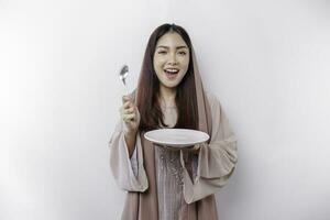 An Asian Muslim woman is fasting and hungry and holding cutlery while looking aside thinking about what to eat photo